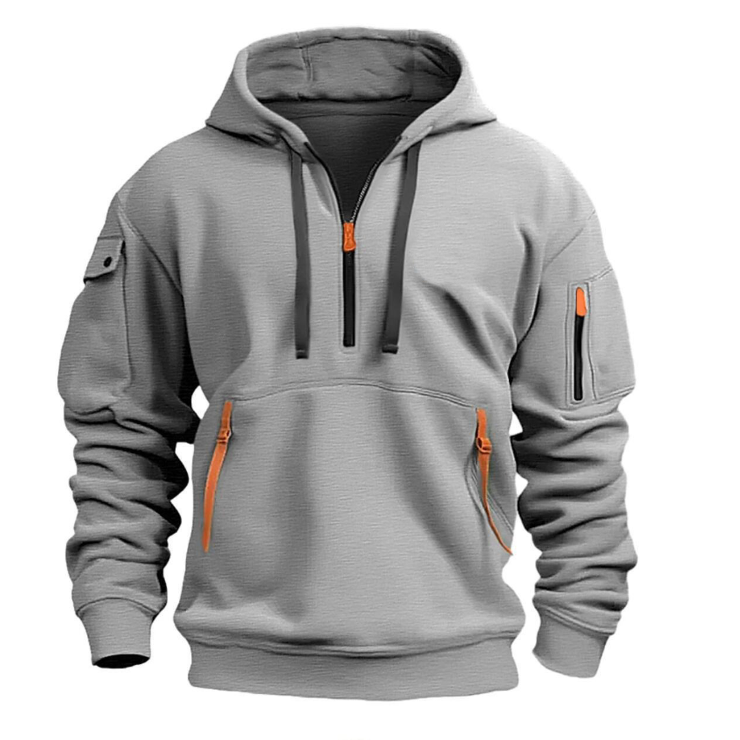 Un sudadera de color gris claro con capucha, cierre en el cuello y detalles en naranja. Presenta varios bolsillos, incluyendo uno en el brazo, y tiene un diseño moderno con un corte cómodo.