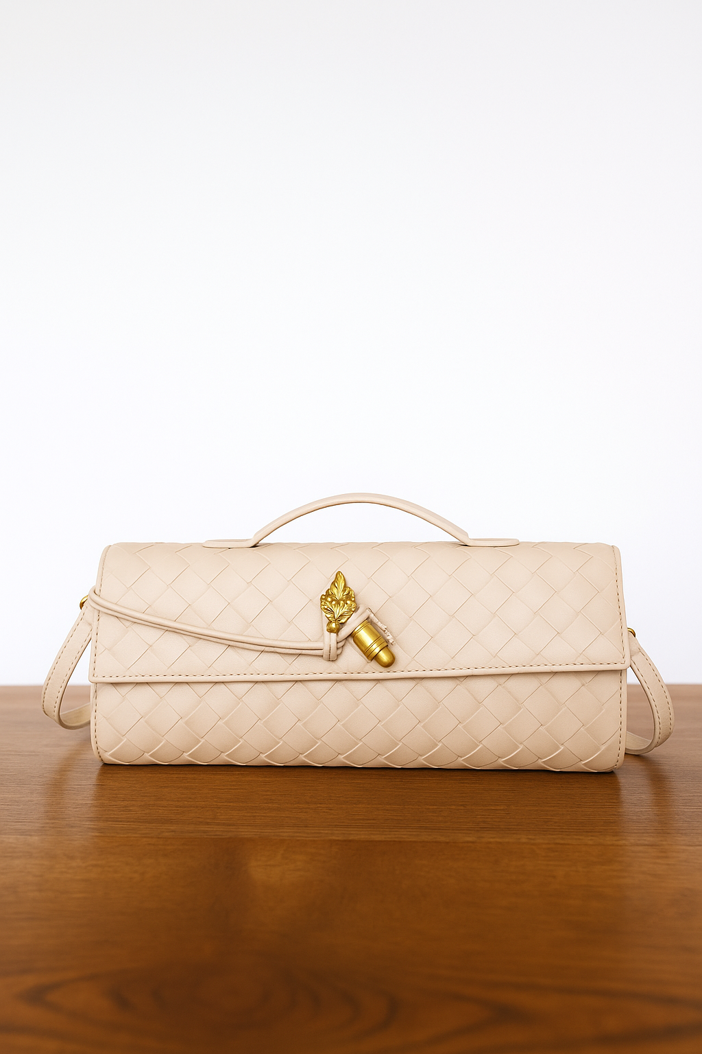 Un bolso de mano de color beige con un diseño de trenzado, presentado sobre un fondo blanco. Tiene un cierre dorado y una correa opcional.